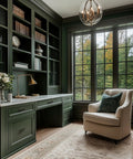 Elegant home office with green cabinets and plush armchair next to large windows overlooking a lush garden