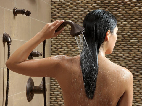 Woman using Cassidy Single Lever Bath Diverter and Transfer Valve Handle Kit in Venetian Bronze for shower, back view.