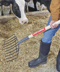 Person using Manure Fork With 30 Inch Hardwood Handle For Moving Manure Mulch Hay And Loose Materials, Heavy Duty 10 Tine Fork, One And A Half Inch Tine Spacing, Welded Tines For Longevity, Comfortable Grip For Yard Work And Easy Cleanup.