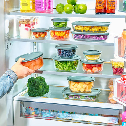 A hand placing a container from the 24 Piece Glass Food Storage Set With Airtight Lids, Leakproof BPA Free Meal Prep Containers in a fridge.