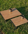 Ultralight Compact Mini Beach Picnic Folding Aluminum Table With Carry Bag Nature Finish Flat Surface Durable Hinges Two Size Options S And M For Sand And Picnics with two sizes shown on grass, each holding a mug.