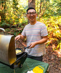 Person cooking outdoors with 12 Count Camping Egg Keeper For Outdoor Cooking And Travel Durable Compact Lightweight Storage Container.