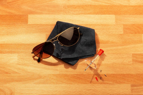 Eyeglass Repair Tool Kit With Small Screwdriver, Spare Screws, Magnifying Glass, Screw Guide, And Universal Storage Pouch For Quick Fixes To Reading Glasses And Sunglasses On The Go displayed with sunglasses on a cloth