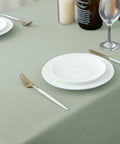 54x54 Inch Sage Square Tablecloth, Linen Like, Water Resistant And Washable on dining table with plates and cutlery