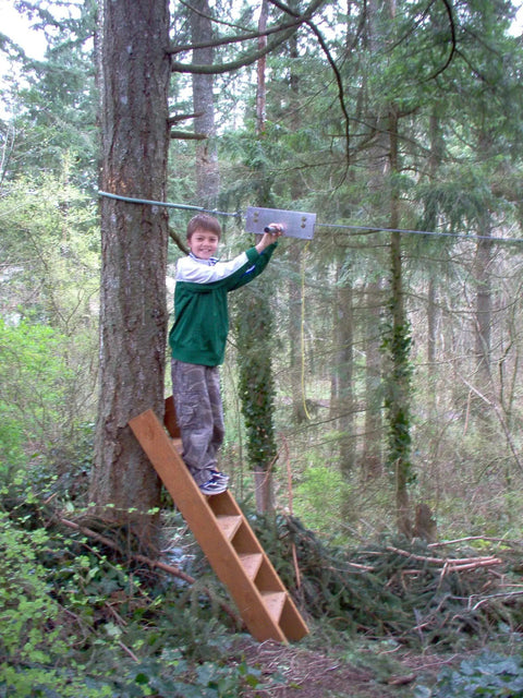 Child using Backyard Zip Line Kit With 100 Foot Cable And Trolley Heavy Duty 350 Lb Capacity Aluminum Handle in forest