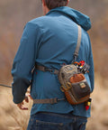 Person wearing Vertical Fly Fishing Chest Pack With Zippered Main Compartment And Interior Pocket Low Profile Tidal Blue Accessory Loops And Belt Loop Attachment For Quick Hands Free Fly Box Storage On The Water, engaged in fishing outdoors.