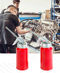 Front view of two red metal pump oil cans with silver tops and levers in an auto repair workshop.