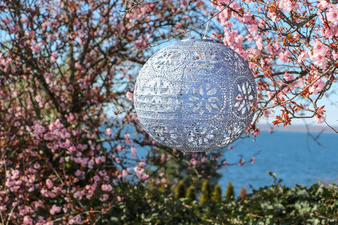 Boho Outdoor Solar Lantern With Weatherproof Tyvek Fabric hanging among cherry blossoms, showing intricate details against a blue sky.