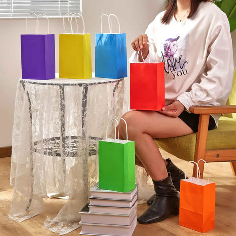 Rainbow Gift Bags With Handles Set 24 Pack 8 Inch Multi Color Paper Party Favor Bags displayed on table with person holding red bag