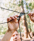 Person adjusting a Taut Line Kit With 550 Paracord For Hanging Gear On A Travel Clothesline Heavy Duty 50 Ft Reflective Paracord.