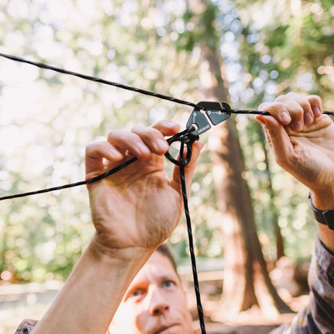 Person adjusting a Taut Line Kit With 550 Paracord For Hanging Gear On A Travel Clothesline Heavy Duty 50 Ft Reflective Paracord.