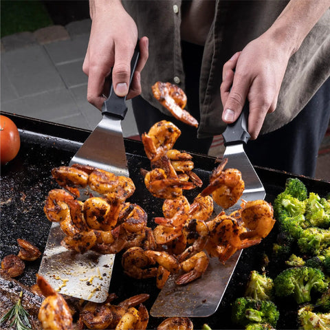 Person using Professional 22 Piece Griddle And BBQ Tool Kit Stainless Steel Dishwasher Safe spatulas to flip shrimp on grill