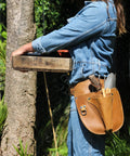 Durable Leather Garden Tool Belt For Women on person holding tools in a garden, showing adjustable fit and compartments.