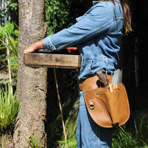 Durable Leather Garden Tool Belt For Women on person holding tools in a garden, showing adjustable fit and compartments.