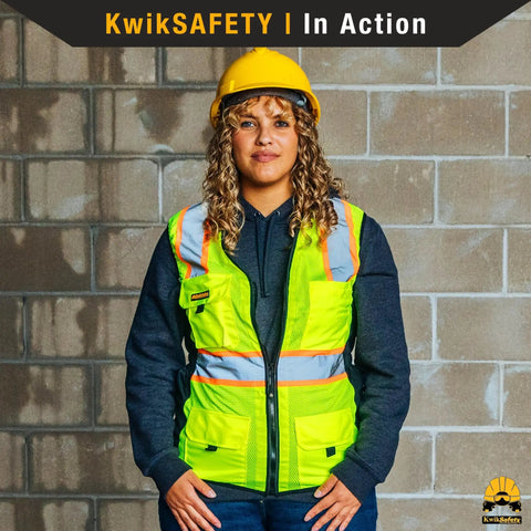 Woman wearing yellow Womens Hi Viz Safety Vest With 9 Pockets, Class 2 Reflective ANSI OSHA Rated, hard hat, standing against wall.