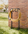 Freestanding Heavy Duty Garden Hose Holder Stand with Rustproof Steel Build and Handy Tool Hooks installed near brick wall.