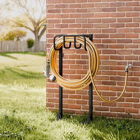 Freestanding Heavy Duty Garden Hose Holder Stand with Rustproof Steel Build and Handy Tool Hooks installed near brick wall.