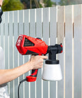 Person using Handheld HVLP Spray Gun With Adjustable Airflow And 600W Power For Home Projects Three Spray Patterns And Four Nozzles on fence