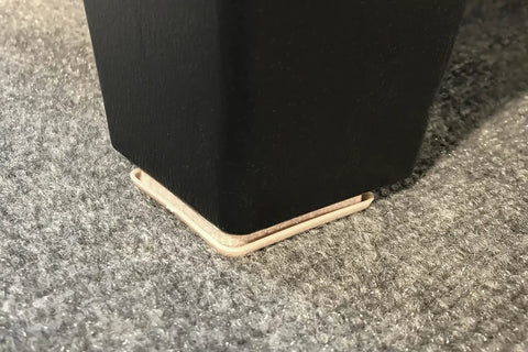 No Sweat Top Tier 2 Inch Square Furniture Sliders with Self Adhesive Backing under a black table leg on soft floor.