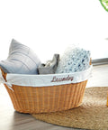 Rattan Laundry Basket With Easy Carry Handles And Removable White Cotton Liner, filled with pillows, on a woven rug.