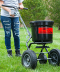 Person using 50 Lb Capacity Push Broadcast Spreader For Lawns And Gardens, Easy Push Handle, Durable Heavy Duty Frame, Model P20-500BH