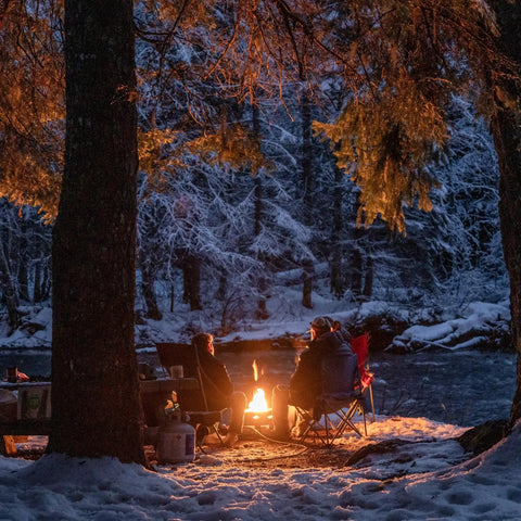 Two people enjoying Smokeless Propane Fire Pit 19 Inch Portable Firebowl 58K BTU With Self Igniter Cover in a snowy forest