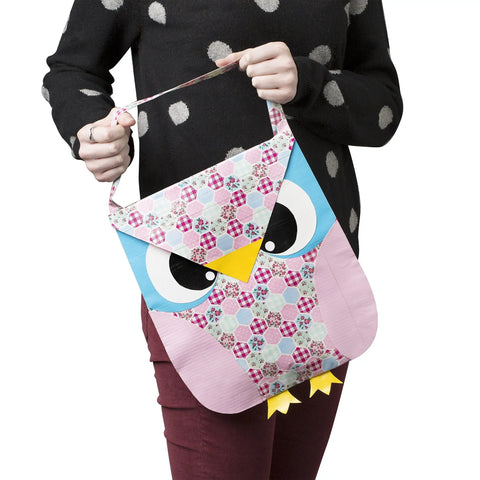 Person holding an owl-shaped, colorful bag with a patchwork pattern and a strap.