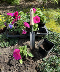 Rock N Root Trowel For Tight Spaces And Deep Digging in soil with pink flowers, showcasing durable ash handle and steel blade.