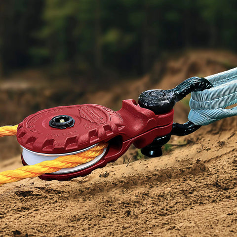 Close-up of a red 10 Ton Snatch Block With Easy Grip Handle For Offroad Recovery Heavy Duty Winch Accessory in use on rugged terrain.