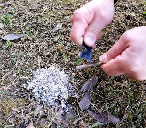 Hands using 3.15 inch ferro rod with Emergency Fire Starter Kit With Pre Shaved Magnesium, 3.15 Inch Ferro Rod, And 4 Inch Waxed Rope In Waterproof Tin For Quick Safe Fires, Ultimate Survival Gear For Camping And Hiking on ground.