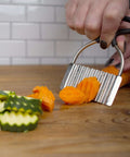 Close-up of stainless steel crinkle cutter with rubber handle slicing orange carrot on a wooden board
