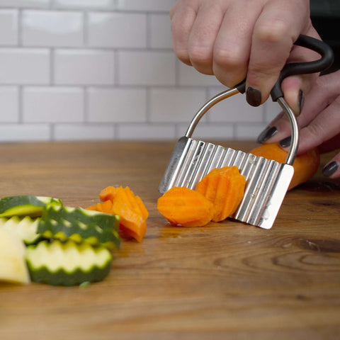 Close-up of stainless steel crinkle cutter with rubber handle slicing orange carrot on a wooden board