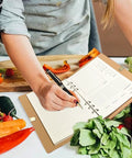 A person using the Leather Recipe Book With Index Pages And Templates, The Ultimate Recipe Notebook For Recording Your Own Dishes, Blank Cookbook To Organize Flavorful Creations, Waterproof Cover For Everyday Kitchen Use, alongside fresh vegetables in a kitchen.