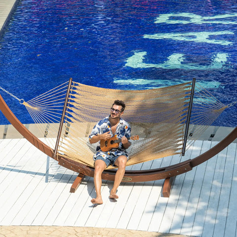 Person relaxing on Caribbean Rope Hammock 10.5 Ft Double Outdoor Hammock With Spreader Bars Hand Woven Polyester by poolside