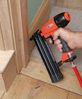 Real Deal Air Brad Nailer With Quick Release Bottom Load Magazine And 1000 18G Type 180 Brads To Knock Out Woodworking Projects In Bold Orange Carry Case, in use on wooden trim.