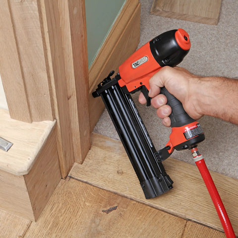 Real Deal Air Brad Nailer With Quick Release Bottom Load Magazine And 1000 18G Type 180 Brads To Knock Out Woodworking Projects In Bold Orange Carry Case, in use on wooden trim.