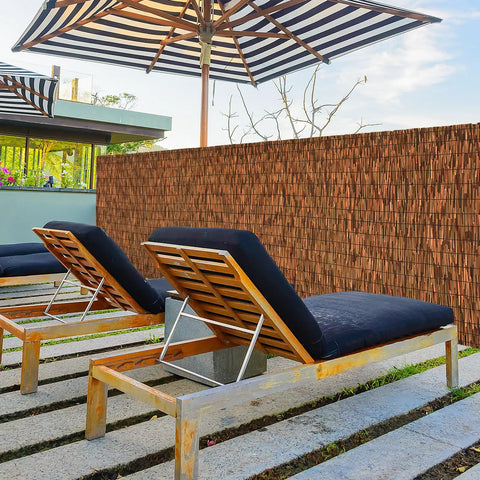 Brown 6 Ft Reed Fencing Roll 16.4 Ft Long Outdoor Privacy Screen bordering a sun lounger area, ideal for patios or yards.