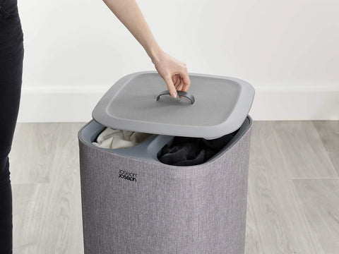Person opening Tota Laundry Hamper With Dual Compartments And Lid, 60 Liter Separation Basket with gray exterior in a room.