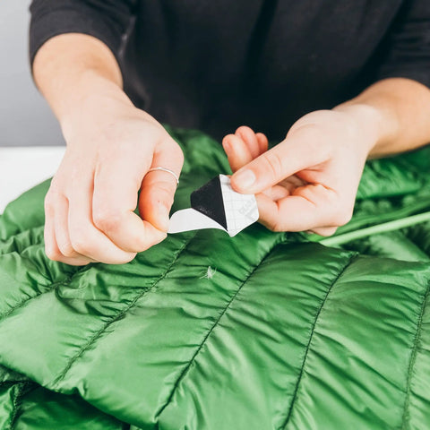 Applying Hex Peel And Stick Repair Patches Kit With Two 2.5 Inch And Two 1.5 Inch Patches In Clear And Black on green down jacket