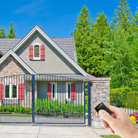 Hand holding Single Button Gate Opener Remote for Automatic Gate System Black FM135 Compatible in front of gated house