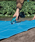 User trimming a blue tarp with Badass Compact 12V Max Lithium Ion Cordless Multi Cutter in a field.