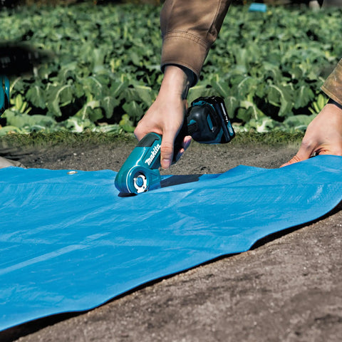 User trimming a blue tarp with Badass Compact 12V Max Lithium Ion Cordless Multi Cutter in a field.