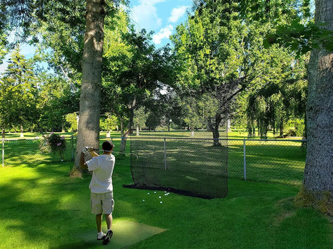 Golfer using Beefy 10x10ft Heavy Duty Golf Practice Net With High Impact Nylon Netting in a backyard setting.