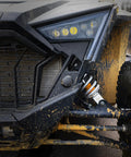 Close-up of muddy off-road vehicle front, showcasing headlight and suspension system, highlighting rugged terrain capabilities.
