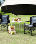 Two black Oversized Directors Camping Chairs With Side Table set up next to a picnic table outdoors on grass.