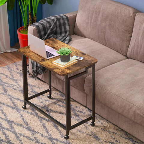 Folding Rolling Computer Desk For Small Spaces by couch, Rustic Brown and Black Finish, with laptop, plant, and book on top.