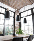 Modern industrial dining area with black pendant lights, brick walls, and large windows overlooking city view.