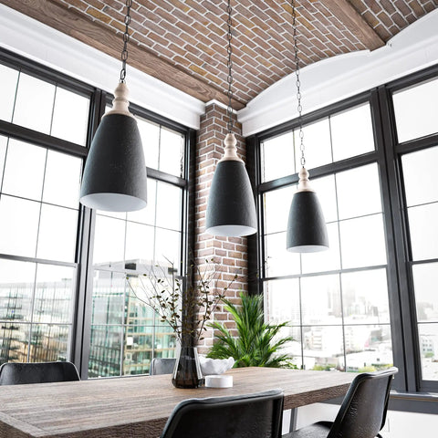 Modern industrial dining area with black pendant lights, brick walls, and large windows overlooking city view.