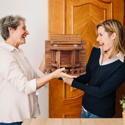 Two people holding a Crescent Wooden Squirrel Feeder Table for outdoor use, showcasing the picnic table style and sturdy structure.