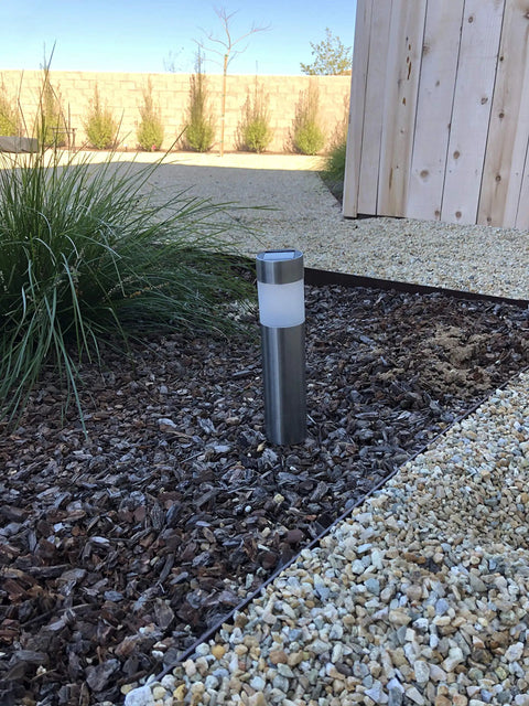 Single solar bollard light installed in garden bed showcasing Six Pack Solar Bollard Path Lights Outdoor Stainless Steel Warm White LED Landscape Lighting For Backyard Lawn Patio Waterproof Durable Silver Finish With Easy Ground Install.